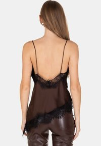 Donna con capelli lunghi che indossa una canottiera in raso marrone con bordo in pizzo nero e pantaloni in pelle marrone, vista da dietro.