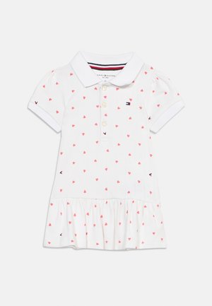 Robe polo blanche à manches courtes avec motif de cœurs roses, patte de boutonnage, ourlet à volants et petit logo brodé sur la poitrine et les manches.