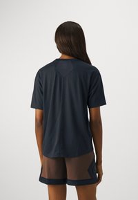 T-shirt en coton bleu marine à manches courtes, avec un empiècement en forme de losange. Le dos présente un patch logo discret près de l'encolure.
