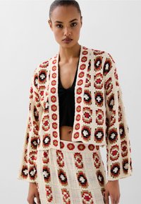 Gehaakte cardigan met een geometrisch patroon in rood, zwart en crème. Heeft een cropped pasvorm, open voorkant en kimono-stijl mouwen.