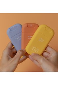 Drei Flaschen Handdesinfektionsmittel: helllila, orange und gelb, mit glatten, matten Oberflächen und abgerundeten Deckeln. Die Etiketten zeigen die Produktnamen.