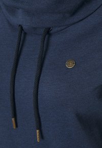 Tummansininen huppari, jossa on suppilon muotoinen kaulus, mustat nyörit, kultaiset metallikoristeet ja teksturoitu kangas. Logo on esillä rinnassa.