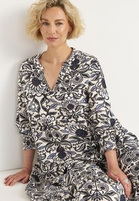 Kleid mit floralem Muster in Creme, Marineblau und Blau. V-Ausschnitt mit elastischen Ärmeln und geraffter Taille. Weicher, strukturierter Stoff.