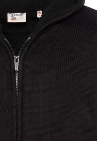 Sweat à capuche zippé noir côtelé avec intérieur doublé en polaire. Comprend une fermeture éclair argentée et une étiquette cousue dans le col. Taille L.