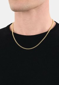 Collana in oro a due strati, con un design piatto e linkato. Indossata sopra un maglione nero a maglia con scollatura a girocollo.