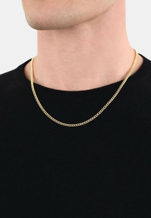 Goldene Kettenhalskette mit zwei Lagen, die ein flaches, verknüpftes Design aufweist. Getragen über einem schwarzen Strickpulli mit Rundhalsausschnitt.