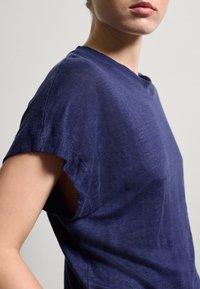 Marineblaue kurzärmelige T-Shirt aus leichtem Stoff, mit lässiger Passform und subtiler Textur, rundem Halsausschnitt und aufgerollten Ärmeln.