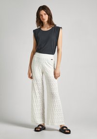 Top corto de manga corta gris oscuro, pantalones anchos blancos con un patrón y detalle de acento, y chanclas negras deslizables. Textura suave y corte relajado.