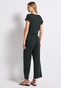 Černý overal s krátkými rukávy, kulatým výstřihem a detailem otvoru na zádech. Obsahuje elastický pas a široké nohavice. Minimalistický design.