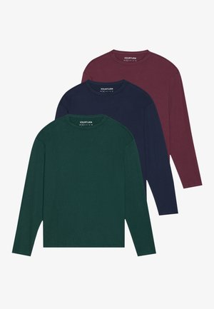 Chemises à manches longues bordeaux sur deux silhouettes, accompagnées de pantalons noirs et de jeans bleu clair. Les deux portent des baskets ; une chemise est nouée à la taille.