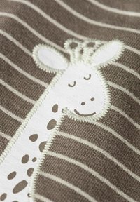 Tissu rayé brun et blanc avec un détail d'une girafe souriante cousue, comprenant son visage et son cou, dans des tons doux de blanc et beige.