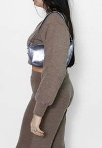Metalen zilveren handtas met een slank ontwerp, een veilige ritsluiting en een gebogen vorm, gecombineerd met een beige, gebreide cropped trui en broek.