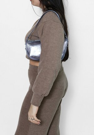 Borsa a tracolla metallica argento con design elegante, chiusura con cerniera sicura e forma curva, abbinata a un maglione corto lavorato a maglia beige e pantaloni.