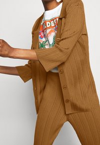 Brun ribbade stickade tvådelade outfit bestående av en knäppning fram kortärmad skjorta och matchande tapered byxor med en texturerad yta.