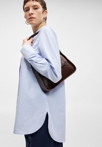 Ανοιχτό μπλε πουκάμισο με ρίγες και μακριά μανίκια, διακοσμημένο με δαντέλα, συνδυασμένο με μια σκούρα καφέ δερμάτινη τσάντα. Το πουκάμισο έχει καμπυλωτό στρίφωμα.