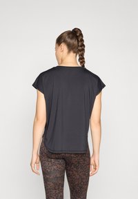 Black short-sleeve top made of lightweight fabric, featuring a relaxed fit and curved hem. Paired with brown leopard print leggings.