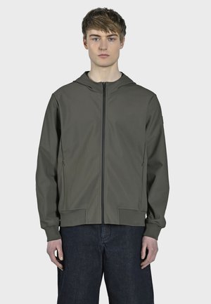 Veste à capuche vert olive, en tissu léger, fermeture éclair, deux poches avant, poignets et ourlet côtelés. Le modèle se tient devant un fond uni.