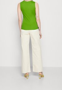 Groen mouwloos topje gecombineerd met roomwitte wijde broekspijpen. Opvallende sandalen met doorzichtige hak en groene accenten, en witte zakdetails op de broek.