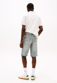 Light blue denim shorts with a straight cut, featuring two rear pockets and a subtle fade; paired with a white short-sleeve shirt and sneakers.