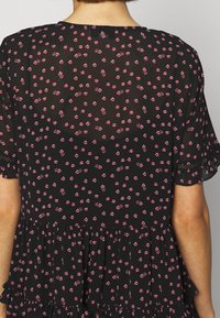 Czarna sukienka z drobnym różowym kwiatowym wzorem, z falbanami na rękawach i dole. Przezroczysta tkanina, lekka tekstura i warstwowy krój.