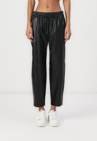 Zwarte leren jogger-stijl broek met een elastische tailleband, een trekkoord en zijzakken met rits, gecombineerd met witte sneakers.