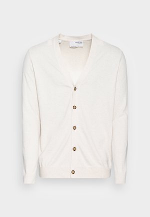 Cárdigan color crema con escote en V, siete botones marrones en el frente y puños acanalados. Hecho de una tela ligera y texturizada.