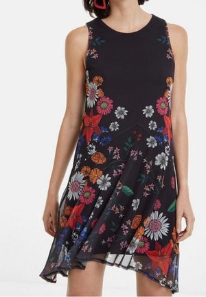 Ärmelloses schwarzes Kleid mit buntem Blumenmuster, rundem Ausschnitt und asymmetrischem Saum, getragen von einer Person mit roten Ohrringen.