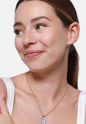 Collana in oro rosa con pendente rettangolare in madreperla. Il modello indossa una maglietta bianca, mettendo in risalto il dettaglio iridescente della collana.