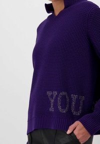 Maglione viola lavorato a maglia con collo alto, orlo a coste e la scritta "YOU" arricchita con strass sulla parte anteriore inferiore.