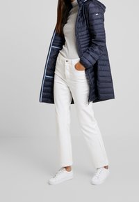 Marineblå dunjakke med hætte, med vandret syninger og lyseblå inderside. Sættes sammen med en grå turtleneck, hvide lige bukser og hvide sneakers.