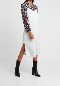 Abito slip in satin bianco con spaccature laterali, abbinato a una camicetta nera a maniche lunghe con fiori nelle tonalità di rosa e verde. Stivali neri con tacco alla caviglia.