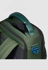 Borsa in tessuto verde con base nera, caratterizzata da un design strutturato, un manico verde liscio, dettagli in metallo e un paio di occhiali da sole neri all'interno.