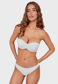 White bandeau bikini with textured pattern and cut-out detailing. Low-rise bikini bottoms with a smooth finish complement the top.