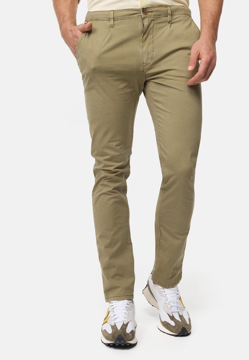 Chinos khaki avec une coupe slim, fabriqués en tissu mélangé coton, dotés de poches avant et d'une braguette zippée, associés à des baskets blanches et grises.