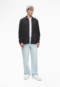 Σκούρο γκρι πουκάμισο με τσέπη, φορεμένο πάνω από ένα λευκό μπλουζάκι. Ανοιχτό μπλε τζιν σε ευθεία γραμμή και λευκά sneakers, και πάνω από όλα, ένα γκρι σκουφάκι.