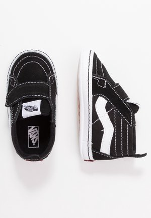 Black and white toddler Vans sneakers with velcro straps, white side stripe, and visible brand logos, shown from top and side views on white background.