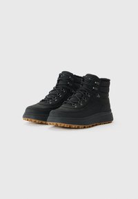 Black waterproof boots feature a padded collar, metal eyelets, and a rubber sole with deep treads for grip. Textile upper with a smooth finish.