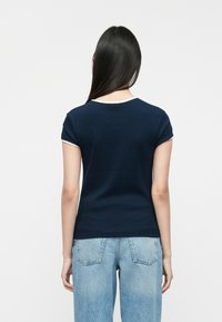 Ναυτικό μπλε βαμβακερό T-shirt με εφαρμοστή σχεδίαση, καμπυλωτά μανίκια και λευκή επένδυση γύρω από το λαιμό. Φορεμένο με ανοιχτό μπλε τζιν.