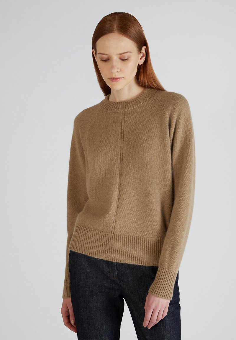 Maglione a maglia marrone chiaro con scollatura tonda, polsini e orlo a coste. Presenta una trama sottile e una silhouette aderente. Indossato con jeans scuri.