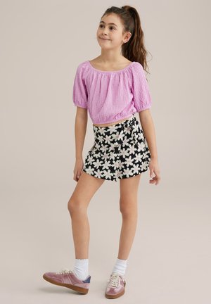 Top rosa strutturato con maniche a palloncino abbinato a una gonna a portafoglio nera con fiori. Completato con sneakers rosa e calzini bianchi.