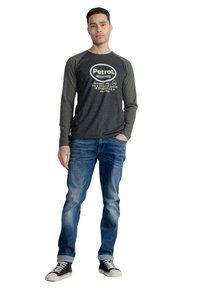 Langærmet grå og grøn raglan skjorte med hvidt trykt tekst, parret med blå jeans og sorte sneakers med hvide såler.