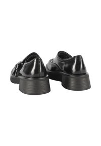 Scarpe in vernice nera con punta tonda, suola texturizzata e tacco basso e spesso. Accenti decorativi di brogue sulla parte superiore.