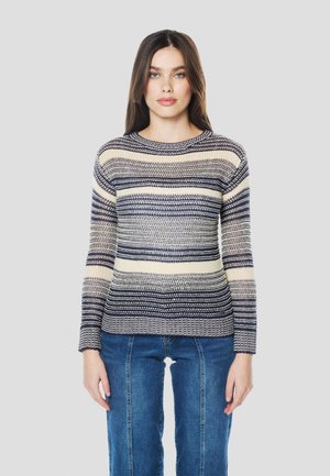 Suéter de punto a rayas en tonos alternos azul marino y beige, con cuello redondo y mangas largas, combinado con vaqueros ajustados.