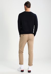 Pull noir à manches longues, chinos kaki et baskets blanches avec des accents rouges. Le pull présente un col rond et des poignets côtelés.