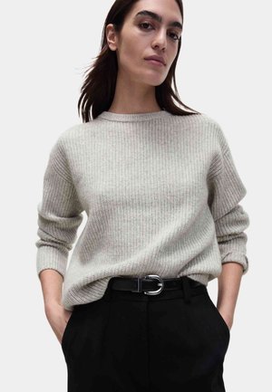 Pull en maille côtelée gris clair avec col rond et manches retroussées, associé à un pantalon noir taille haute et une ceinture noire à boucle argentée.