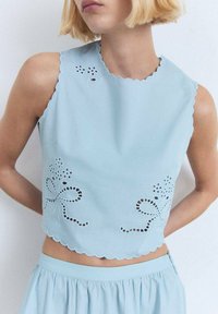 Cropped top azzurro chiaro realizzato in tessuto con bordi ondulati, caratterizzato da fiori ricamati e modelli a fiocco decorativi.