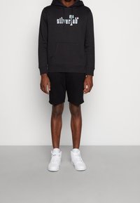 Svart hoodie med "silverTab"-logotyp, framficka och snodd i huvan. Kombinerad med svarta shorts och vita sneakers. Enkelt mönster och passform.