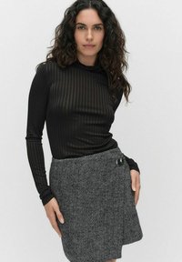 Musta ribattuja pitkähihaista toppia, jossa on korkea kaulus; yhdistettynä teksturoituun harmaaseen houndstooth-hameeseen, jossa on sivutakkipainike.