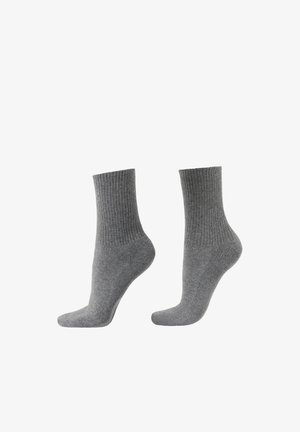 Grijze katoenen sokken met geribbelde manchetten, halflange lengte tot halverwege de kuit, gladde textuur, en verstevigde hiel- en teenzones. Eenvoudig en veelzijdig ontwerp.