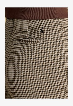 Byxor i brunt och beige hundtandsmönster med texturerat tyg. Har en bakficka och svart broderad detalj ovanför fickan.